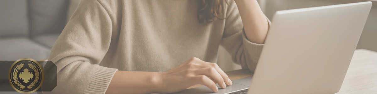 Mulher concentrada usando um laptop em sua casa, sentada à mesa com expressão curiosa, em ambiente iluminado por luz natural.